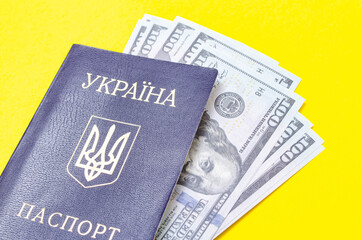 Ukrainian passport on a yellow background. $ 100 dollars are inside the passport at different angles