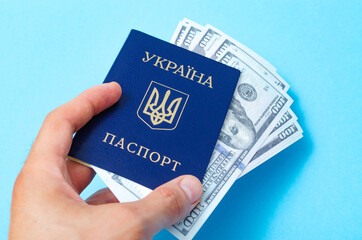 Ukrainian passport on a blue background. Dollars of 100 dollars are inside the passport at different angles. Male hand holds, gives a passport with dollars inside
