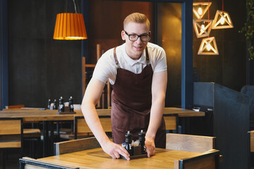 Waiter young man in restaurant, preparing tables for opening after quarantine
