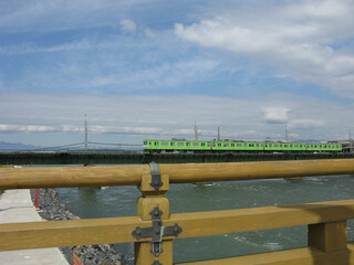 Green train on railway bridge over Uji River. 