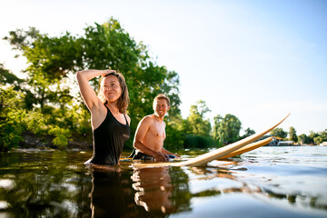 young athletic man and woman are sitting on their surfboards in the water