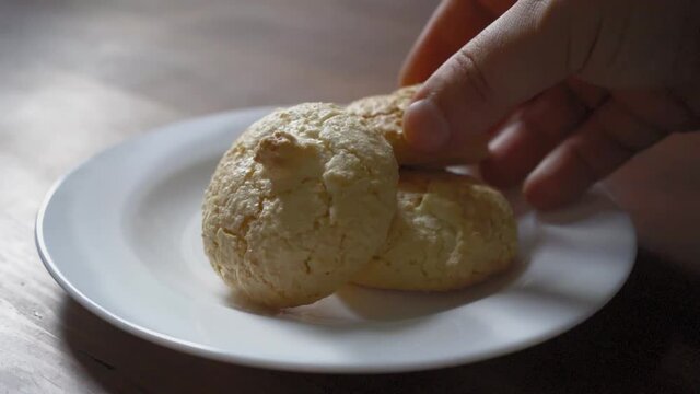 Hands one by one take cookie off the white plate standing on the dark wooden table. Biscuits on the table. Prores 422. 
