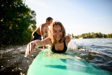 Close-up portrait of cheerful woman lies on surfboard and rows her hands and male instructor supports her
