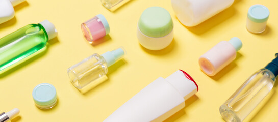 Composition of different sized cosmetic jars and bottles on yellow background. Beauty care concept with copy space