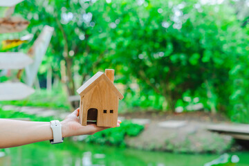 Obraz na płótnie Canvas Woman hand holding a wooden orange house toy, Blurred background is a natural view With green trees