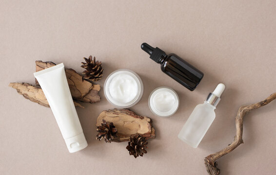 Set eco natural skin and body care beauty products and pine bark and cone on beige background flat lay, top view. Template plastic tube, glass jars and glass bottles with pipette