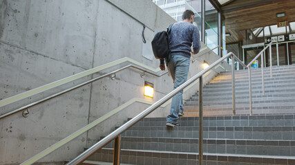 High quality picture of a young man who climbs the stairs at the station and holds a phone in his hands and a backpack on his back. A man hurries on a train, bus, airplane subway, transport 