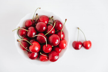 Obraz na płótnie Canvas Fresh juicy red cherries in a white plate on the white wooden background. Top view. Copy, empty space for text