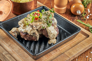Appetizing beef steak with mushroom sauce in a decorative pan on a wooden tray. Wood background. Close up