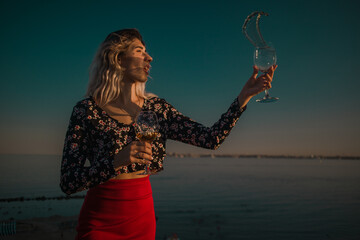young curly blonde fooling around with glasses in hand on a background of sky and sea