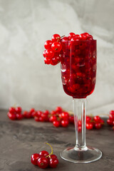 Red currant in a shot glass, the rest is scattered around it on a gray textured background