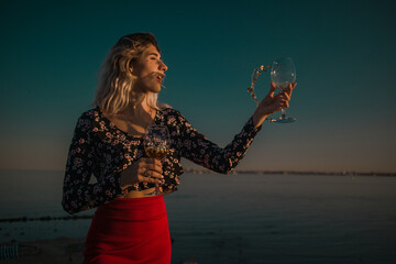 young curly blonde fooling around with glasses in hand on a background of sky and sea