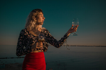 young curly blonde fooling around with glasses in hand on a background of sky and sea