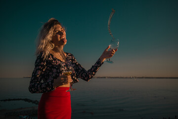 young curly blonde fooling around with glasses in hand on a background of sky and sea