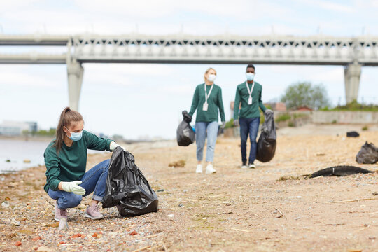 Group of volunteers picking up the rubbish near the bank of the river outdoors