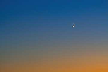 Obraz premium Zunehmder Mond am Abend auf blauem Himmel mit orangenen Abendrot, Sichelmond, 