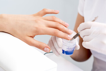 Human hands in protective gloves covering clear varnish to female nails
