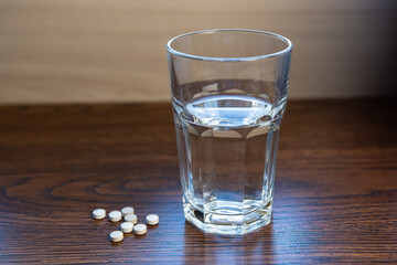 pills lying next to a glass of water on a wooden table