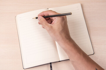 open notebook with black pencil in hand on wooden background top view, school notepad and male hand on a table, a desktop in the office