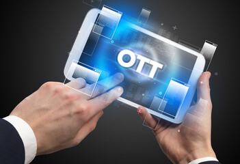 Close-up of a hand holding tablet with OTT abbreviation, modern technology concept