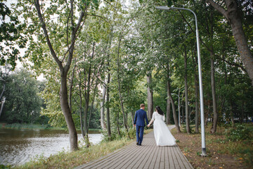 the bride and groom are walking along the park avenue holding hands near the river