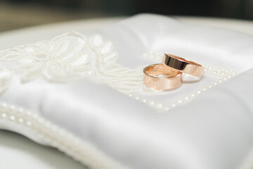 wedding shiny gold rings lie on a white pillow tied with a white ribbon