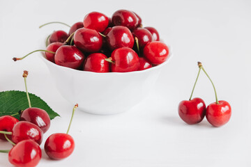Fresh juicy red cherries in a white plate on the white wooden background. Copy, empty space for text