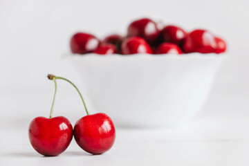 Fresh juicy red cherries in a white plate on the white wooden background. Copy, empty space for text