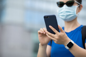 Woman wearing face mask using smart phone on city