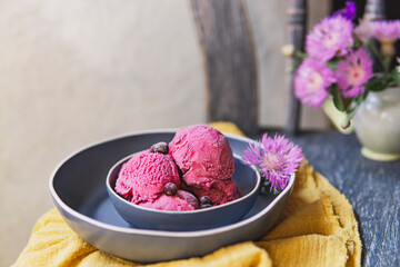 Blackcurrant ice cream or berry sorbet with berries on blue ceramic plate, vintage wooden chair with yellow textile and flowers. Country style, organic raw dessert, healthy food concept. Copy space. - obrazy, fototapety, plakaty