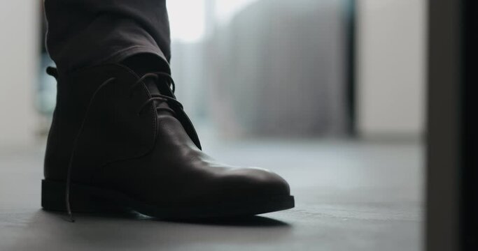 Young man put on his brown leather chukka boots indoor
