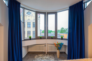 Contemporary interior of luxury flat. Studio apartment. Panorama windows with blue curtains. Decorations.