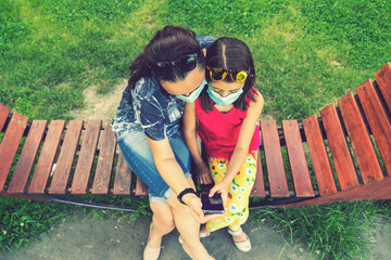 Mom with daughter in the park in medical masks. Family of mom and kid wearing protective medical...