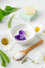 Obraz na płótnie Canvas Vertical image.Bowl of sea salt, purple flower petals, chamomiles, wooden spoon, aloe on the marble table