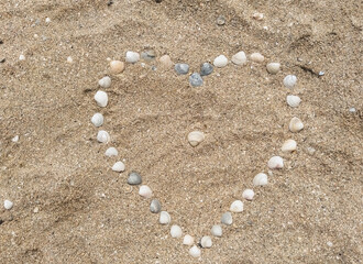 Heart made of sea shells laid out on sea sand. Photograph, top view.