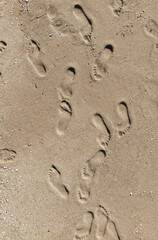 Fototapeta na wymiar Many prints of male feet on the sea sand. Walk barefoot along the shore with footprints. Tourist rest.