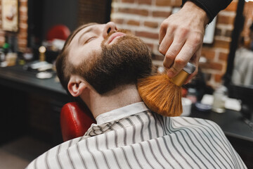 Hairdresser removes hair from client's beard with brush
