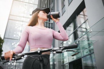 Fototapeta premium Girl on a bicycle drinks from a shaker after a long ride