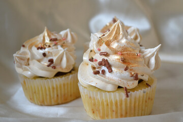 
Tasty cupcake with white and gold cream, with chocolate topping, on a milk background.