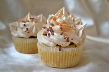 
Tasty cupcake with white and gold cream, with chocolate topping, on a milk background.