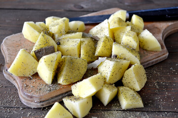 
Potato chopped with spices. Old cutting board, on a dark wooden background. Background.
