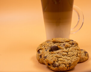 A studio shot of three-layered coffee drink and chocolate chip cookies in orange ombre background