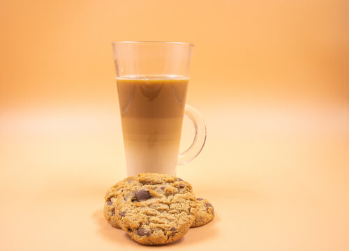A studio shot of three-layered coffee drink and chocolate chip cookies in orange ombre background