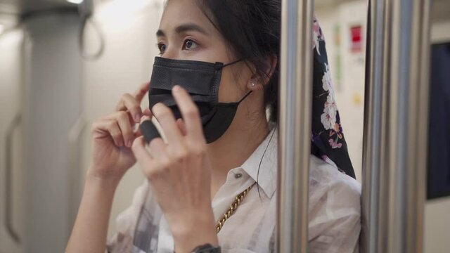 Asian woman adjust her black protective mask, stand at center of train car, metro train station, covid girl inside subway station, New normal lifestyle, self protection, SLOW MOTION