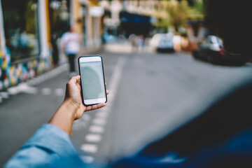 Cropped hand holding modern smartphone device on blurred background of urban setting.Digital mobile...