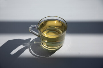 cup of green tea on a white background on a sunny summer day, beautiful shadow from the cup and hand