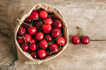 Fresh ripe cherries in a paper bag on wooden background. Top view. Copy, empty space for text