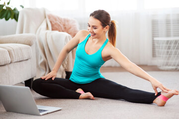 Online home stretching. Slim girl doing fitness routine on floor and watching laptop at home. Copy space