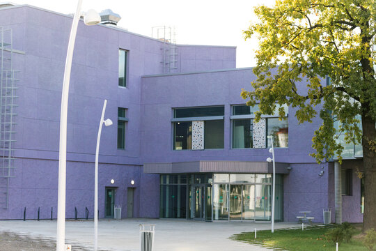 Modern purple building with lawn and trees, lights around. Entrance to low-rise business center