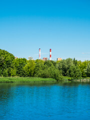 Summer city landscape - pipes and houses near the park on the banks of the city pond